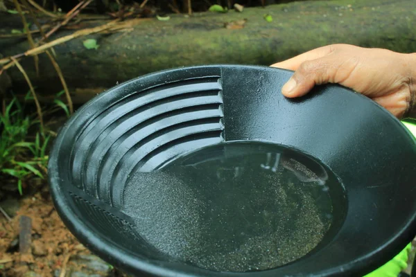 Gold pan full of black sand, under which the gold nuggets are buried