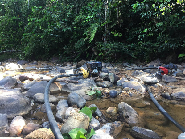 Два водяных насоса для откачки воды для добычи золота, грязь смывает в реку на заднем плане
