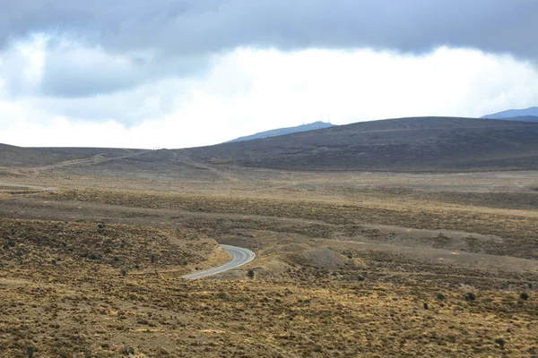 Küçük bir tepenin etrafından giden ve kuru, kayalık bir arazide tekrar kaybolan bir yol — Stok fotoğraf