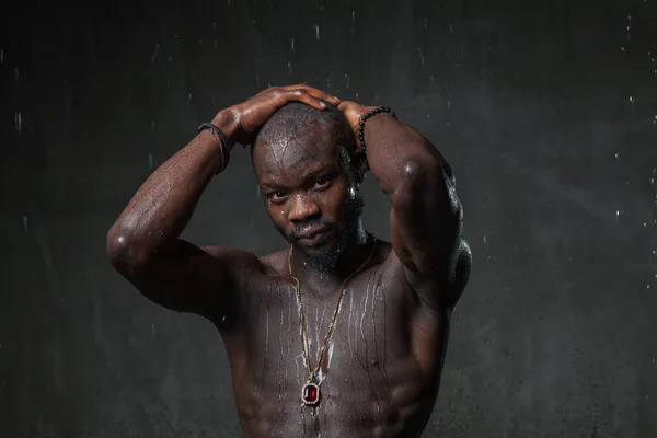 strong  African American young man posing under rain on gray concrete background