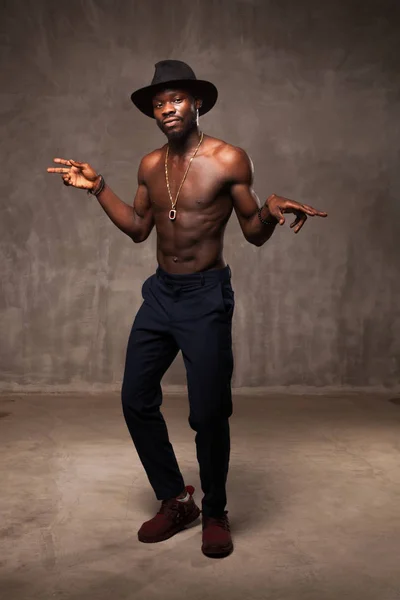 strong African American young man in black hat dancing against grunge concrete background