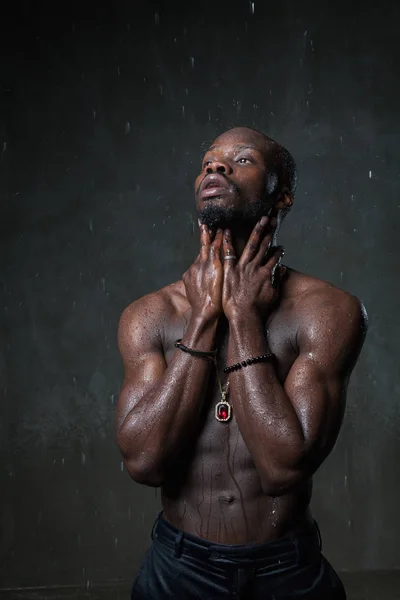 strong  African American young man posing under rain on gray concrete background