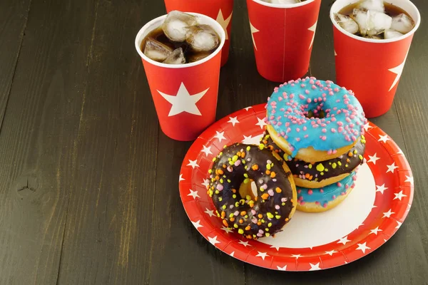 Iced cola in red paper glasses and tasty glazed donuts on dark brown wooden table