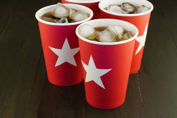 Iced cola in red paper glasses with white stars on dark brown wooden table