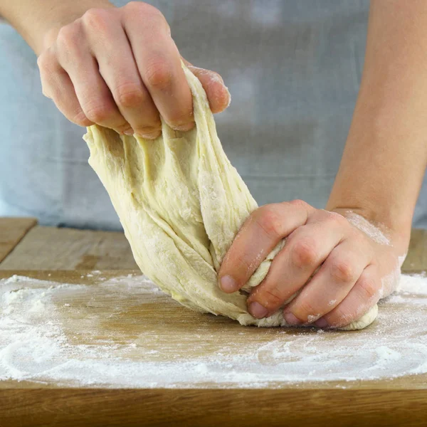 Chef hands kneading raw dough on wooden board