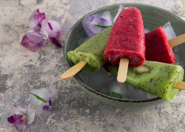 Ev yapımı kivi ve beton zemin üzerine donmuş çiçekli ahududu popsicles