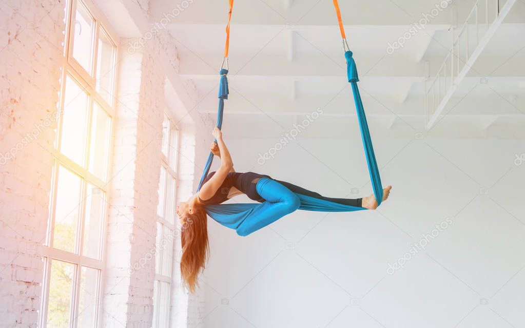young woman doing fly yoga stretching exercises in white gym