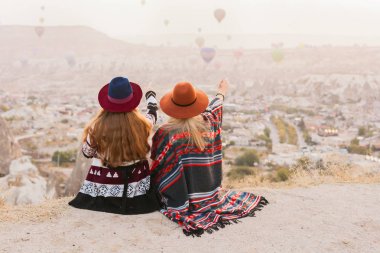 Otantik boho şık tarzı poncho giyen seyahat kadınlar, tatlı ve şapka Kapadokya vadisinde gökyüzünde hava ballons bakıyor. Seyahat ve wanderlust kavramı. Alan arka planını kopyalama.