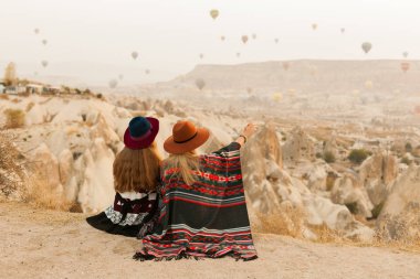 Otantik boho şık tarzı poncho giyen seyahat kadınlar, tatlı ve şapka Kapadokya vadisinde gökyüzünde hava ballons bakıyor. Seyahat ve wanderlust kavramı. Alan arka planını kopyalama.