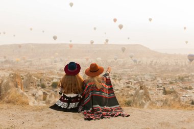 Otantik boho şık tarzı poncho giyen seyahat kadınlar, tatlı ve şapka Kapadokya vadisinde gökyüzünde hava ballons bakıyor. Seyahat ve wanderlust kavramı.