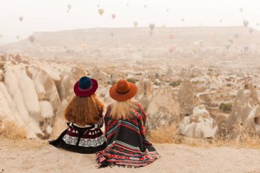 Otantik boho şık tarzı poncho giyen seyahat kadınlar, tatlı ve şapka Kapadokya vadisinde gökyüzünde hava ballons bakıyor. Seyahat ve wanderlust kavramı. Alan arka planını kopyalama.