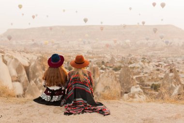 Otantik boho şık tarzı poncho giyen seyahat kadınlar, tatlı ve şapka Kapadokya vadisinde gökyüzünde hava ballons bakıyor. Seyahat ve wanderlust kavramı. Alan arka planını kopyalama.