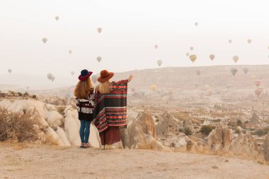 Otantik boho şık tarzı poncho giyen seyahat kadınlar, tatlı ve şapka Kapadokya vadisinde gökyüzünde hava ballons bakıyor. Seyahat ve wanderlust kavramı. Alan arka planını kopyalama.