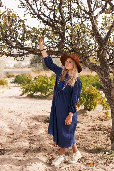 Güzel sarı saçlı genç kadın elma ağacı yakınında mavi etek ve kahverengi şapka giyiyor. Yerel tarım iş büyüme kavramı. Yavaş yaşam otantik yaşam tarzı.