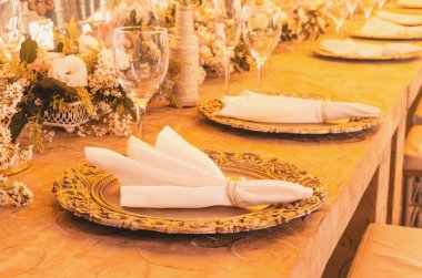 Masa dekorasyonu altın sousplat, peçete, cam bardak ile bazı şişeler, çiçek dekorasyon ve süs eşyaları masa üzerinde el işi.