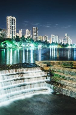 Photo of the Lago Igapo, Londrina - Parana, Brazil. View of the Igapo lake at night, the artificial waterfalls and the city, buildings on background. Leisure place, touristic destination of the city. clipart