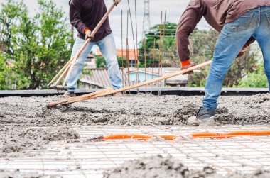 İşçiler bir ev yapım aşamasında levha üzerine beton yayılıyor. Arka bina bir ev, yapısal parçalar. Çelik kiriş ve ev tavanda Boru hattların başka şekilli elektrik şebeke.