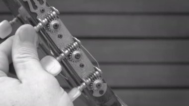 Eski bir akustik gitarı tonlama. Parmaklar akustik gitarın headstock'un tuning mandallarını ve dişlilerini döndürdü. Siyah beyaz görüntüler.