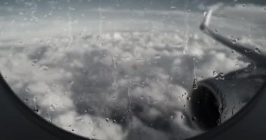 Yağmurda bir uçağın uçuşu. Uçağın penceresinden bak, kanat ve jet motoru, yağmurlu bir gün, ağır bulutların üstünde uçmak, pencere camından süzülen su damlaları. Canlandırma.