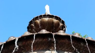 Mavi bir gökyüzünün arka planında, su bronz çeşmenin girintilerinden sorunsuz cayır..