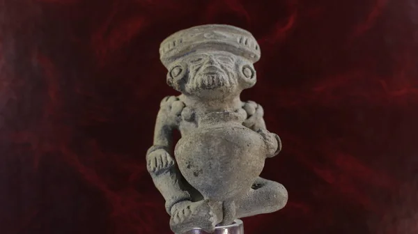 Figurine of a seated man with a jug and with earrings in his ears.