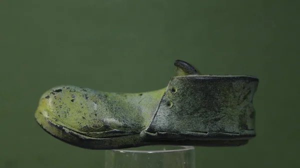 Figurine of an old, green boot, on a green background.