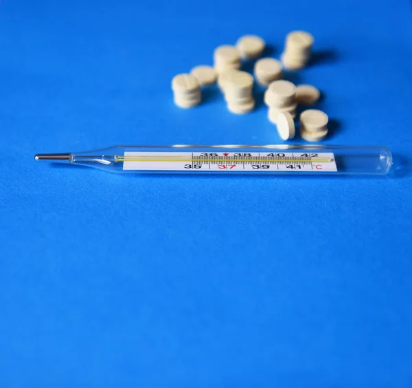 mercury thermometer and pills on blue background