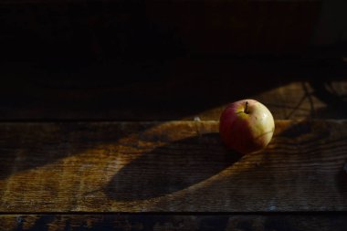Olgun bir elma, gün ışığında tahta bir masanın üzerinde.