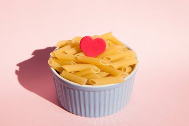 Makarna kase kavramı pişirme pembe arka plan üzerinde kırmızı kalp