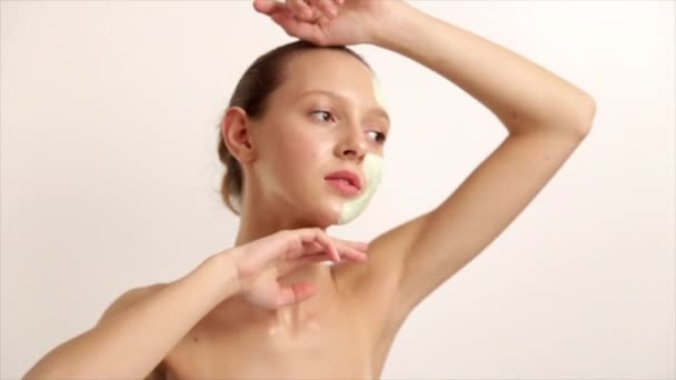 Das junge schöne Mädchen hat eine kosmetische Maske verursacht, weiße Gesichtscreme Hautgesundheit, steht auf einem hellen Hintergrund prores Codec — Stockvideo