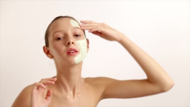 Das junge schöne Mädchen hat eine kosmetische Maske verursacht, weiße Gesichtscreme Hautgesundheit, steht auf einem hellen Hintergrund prores Codec — Stockvideo