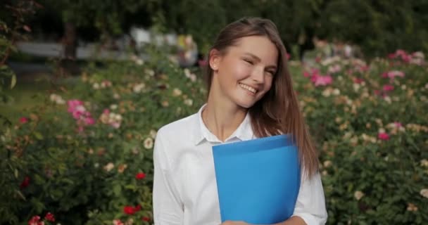 La mujer de negocios controla la ejecución de obras. Joven chica atractiva en gafas de sol en camisa blanca contra flores fondo quita las gafas de sol y mira deslumbrantemente. Codec Prores de cámara lenta — Vídeo de stock