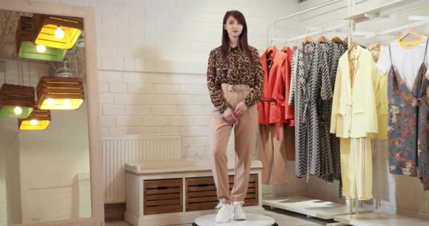 Een mooi meisje draait om haar as op de draaitafel. Toon het model van de kleding. Model in Luipaard shirt en bruine broek 4k — Stockvideo