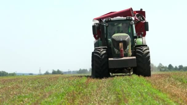 Zelený traktorový vůz s červeným nakladačem v Obilním poli a jasnou modrou oblohou. Prory, pomalý pohyb — Stock video