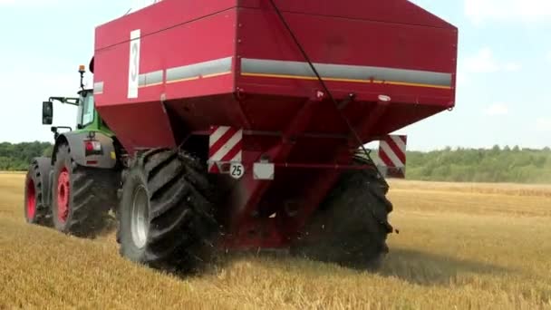 Zielony Traktor z czerwonym ziarna zbiornika jeździ na polu podczas żniw. ProRes, zwolnionym tempie — Wideo stockowe