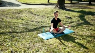 Parktaki Yoga. Yeşil Çimlerde Oturan Lotus Pozisyonundaki Genç Adam. Barış ve meditasyon kavramı. Dualar, Yavaş Hareket