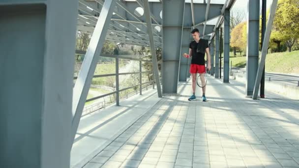 Retrato de un joven en forma con cuerda de salto en la plataforma cerca de bastidores de metal. Fitness Saltar el entrenamiento al aire libre. El tipo salta cerca de los pilares de metal en el fondo del estadio. Vestido con una T negra — Vídeos de Stock