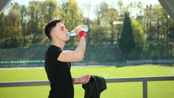 Utmattad ung man torkar svett med handduk från pannan efter träningen. Trött idrottskvinna dricksvatten och vilar nära stadion. Konceptet Sorowako livsstil och sport. ProRes, långsam — Stockvideo