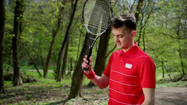 En ung man sätter ett tennisracket på axeln och dricker vatten från en plastflaska för att släcka törst. Konceptet om en hälsosam livsstil, idrott i parken. ProRes, slow motion — Stockvideo