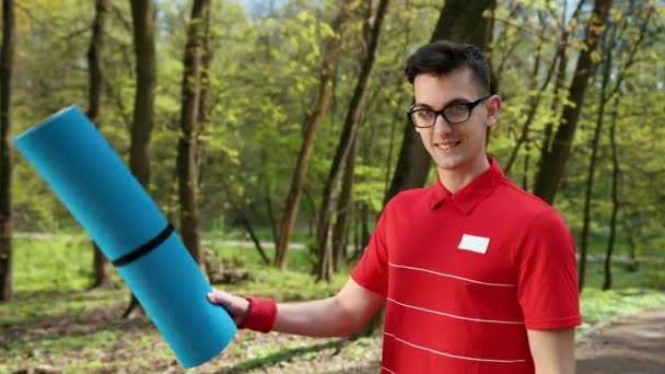 Hübscher junger Mann mit Brille legt seinen blauen Teppich auf seine Schulter und zeigt Zeichen, dass alles in Ordnung ist. — Stockvideo