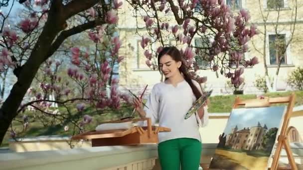 Belle fille artiste peint son tableau sur le fond d'un arbre sakura. Près des femmes, chevalet, os et peintures — Video