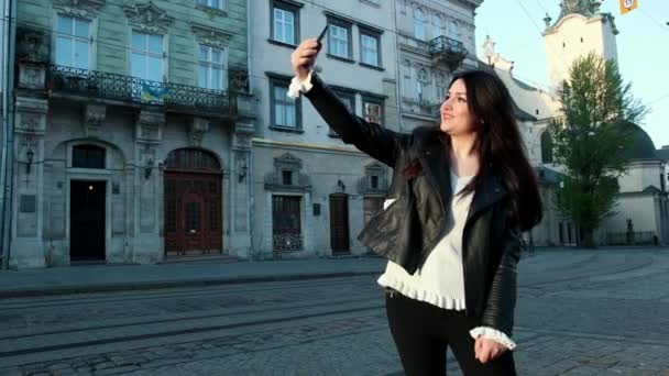 Güzel esmer kadın telefona bakar ve şehirde selfie 'ler alır. İyi kentsel mimarinin arkasında. Bir Blogger blog telefonda canlı yol açar. ProRes, yavaş hareket — Stok video