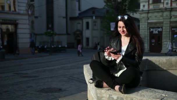 Ευρεία γωνία των όμορφων νέων επιχειρήσεων Καυκάσια γυναίκα με smart messager κάθεται κοντά στο μνημείο. Αργή κίνηση. Προτιμήσεις — Αρχείο Βίντεο