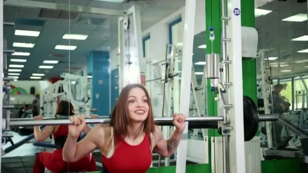 Joven hermosa mujer levanta la barra en el gimnasio y toma poste de metal alrededor de la cabeza — Vídeo de stock