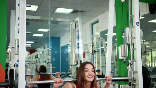 Jovem mulher bonita levanta bar no ginásio e leva pólo de metal em torno da cabeça — Vídeo de Stock