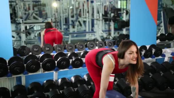 Menina bonita em terno vermelho faz o haltere de exercício de elevação, que segura nas mãos — Vídeo de Stock