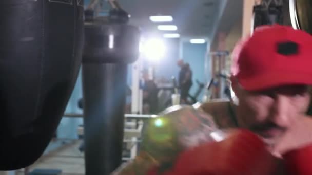 Handsome young man with bare torso in red cap and boxing gloves boxing on goal. — Stock Video