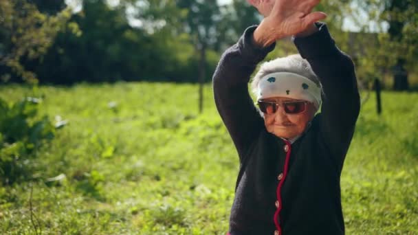 Uma velha mulher usando óculos de sol levanta e abaixa as mãos — Vídeo de Stock
