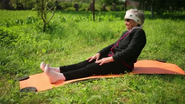 Mujer atleta de 100 años se acuesta en una esterilla de yoga con gafas de sol y se inclina — Vídeo de stock
