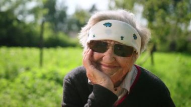 bir çene tutan bir el ile güneş gözlüğü oturan yaşlı bir kadının portresi.